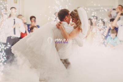 Homme souriant portant un casque audio et un costume sombre, éclairé par une lumière douce sur fond noir.