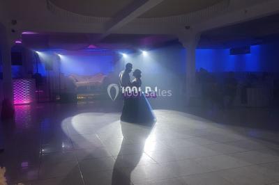 Homme souriant portant un casque audio et un costume sombre, éclairé par une lumière douce sur fond noir.