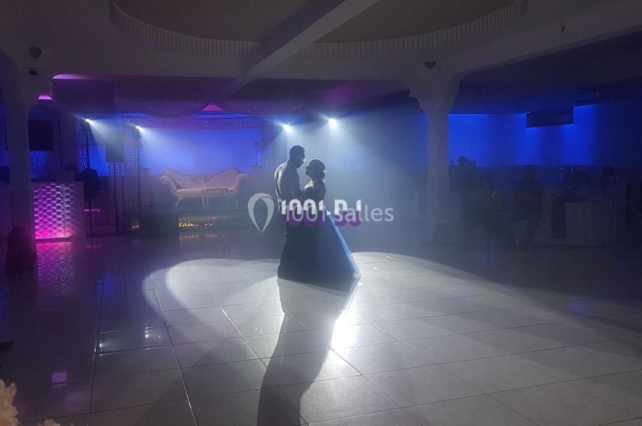 Un couple danse sous des projecteurs dans une salle de réception éclairée par des lumières colorées.