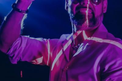 Homme souriant portant un casque audio et un costume sombre, éclairé par une lumière douce sur fond noir.