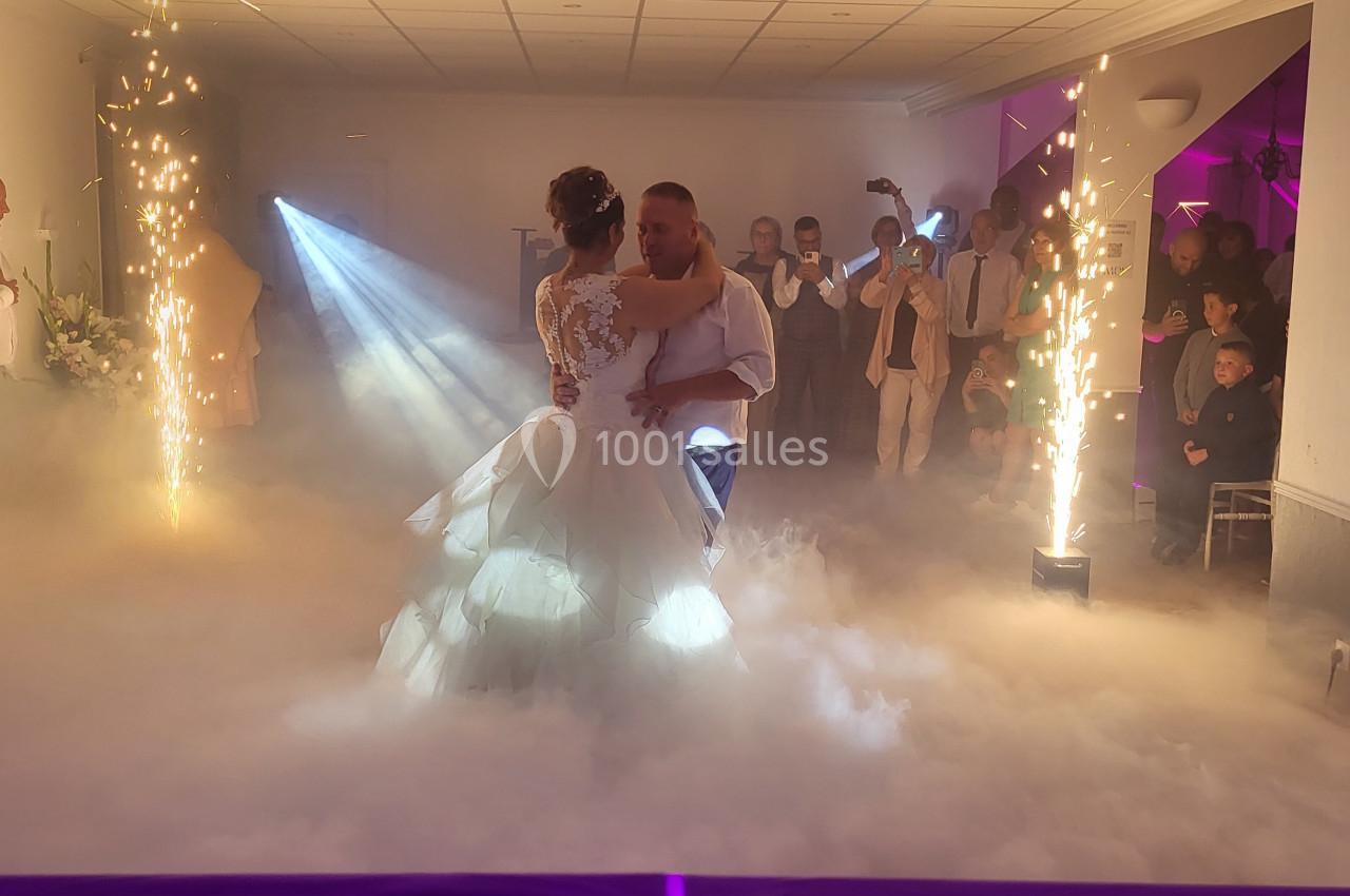 Un couple danse au milieu d'une salle décorée avec des effets de fumée et des étincelles, entouré d'invités.