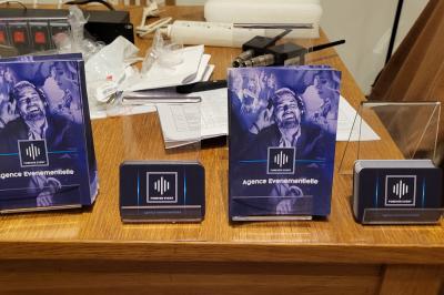 Homme souriant portant un casque audio et un costume sombre, éclairé par une lumière douce sur fond noir.