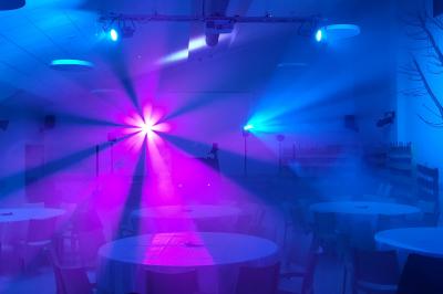 Homme souriant portant un casque audio et un costume sombre, éclairé par une lumière douce sur fond noir.