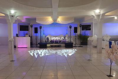 Salle de réception avec piste de danse, éclairage violet, équipement audio et décoration florale.