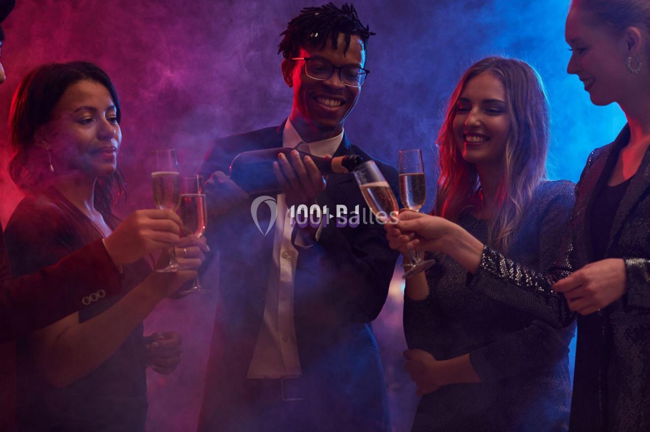 Un groupe de personnes trinque avec des coupes de champagne dans une ambiance festive et éclairage coloré.