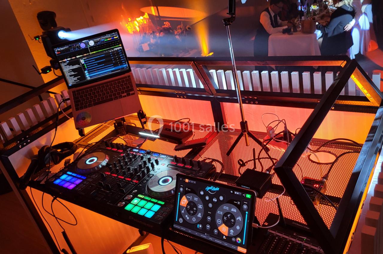 Poste de DJ avec platines, ordinateur portable et tablette, éclairé par des lumières colorées dans une ambiance festive.