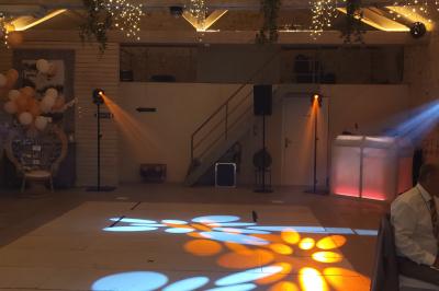Salle de réception avec piste de danse, éclairage violet, équipement audio et décoration florale.