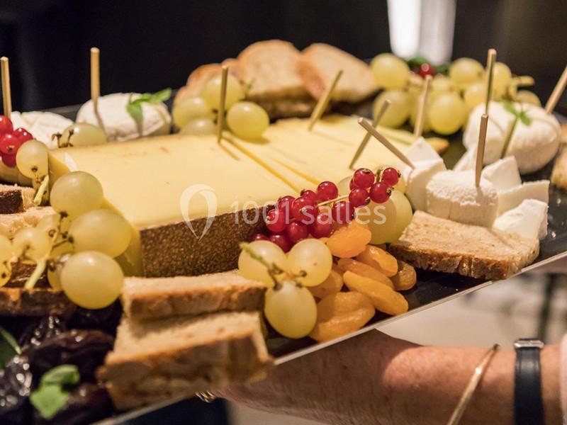 Plateau de fromages variés accompagné de fruits frais, pain et fruits secs, présenté sur un plateau noir.