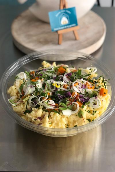 Salade de pommes de terre garnie de légumes colorés, herbes fraîches et rondelles de poireaux dans un bol transparent.