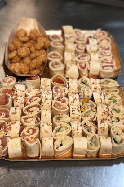 Plateau de wraps variés garnis de légumes, fromage et charcuterie, accompagné de bouchées apéritives dorées.