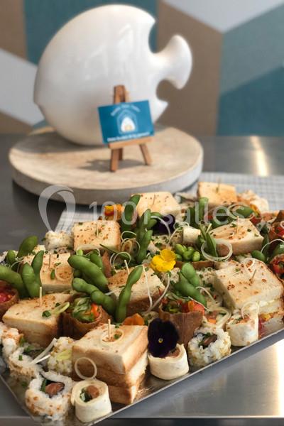 Plateau de bouchées variées comprenant des sandwichs, sushis et légumes, présenté sur une table en métal.