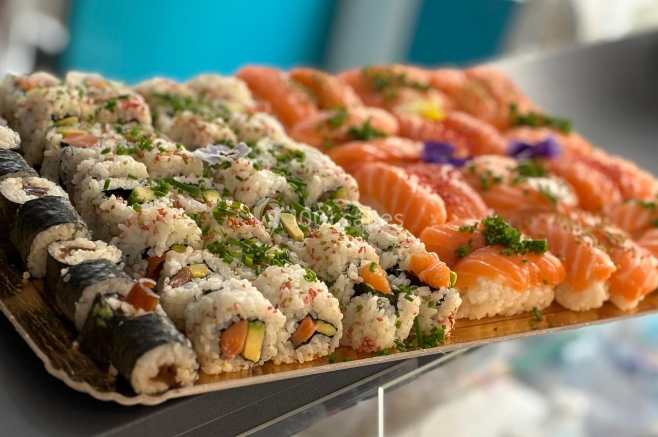 Plateau de sushis variés comprenant des makis, des california rolls et des sashimis au saumon, présenté sur un comptoir.