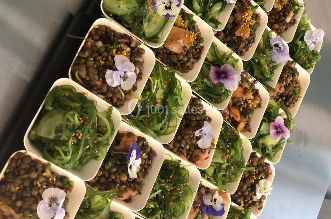 Assortiment de verrines garnies de lentilles, algues, saumon et fleurs comestibles, disposées sur un plateau.