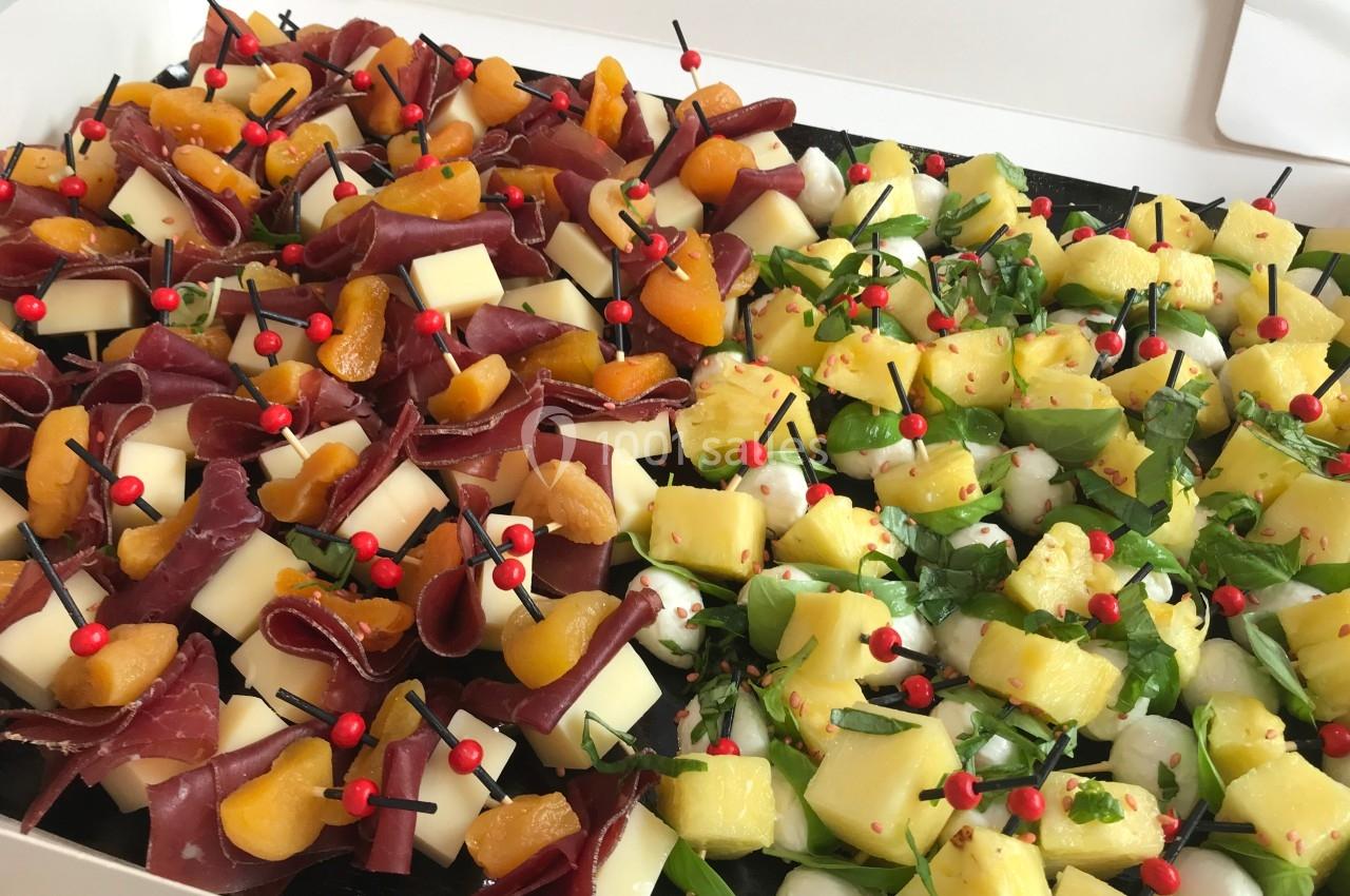 Plateau de brochettes apéritives variées avec fromage, fruits, charcuterie et herbes fraîches.
