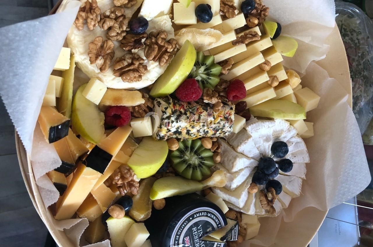 Plateau garni de fromages variés, fruits frais, noix et un fromage roulé aux herbes, présenté sur du papier parchemin.