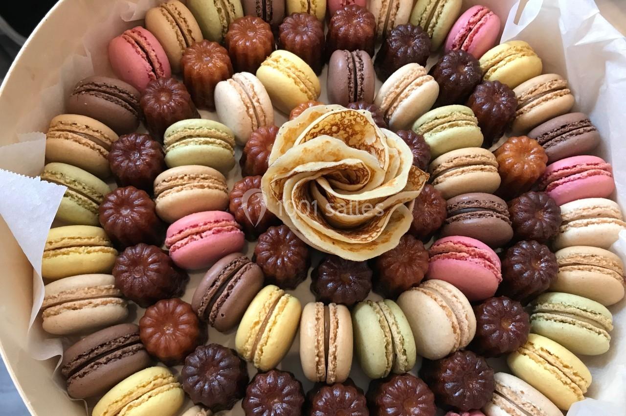 Assortiment de macarons colorés et de cannelés disposés en cercle autour d'une rose en crêpe.