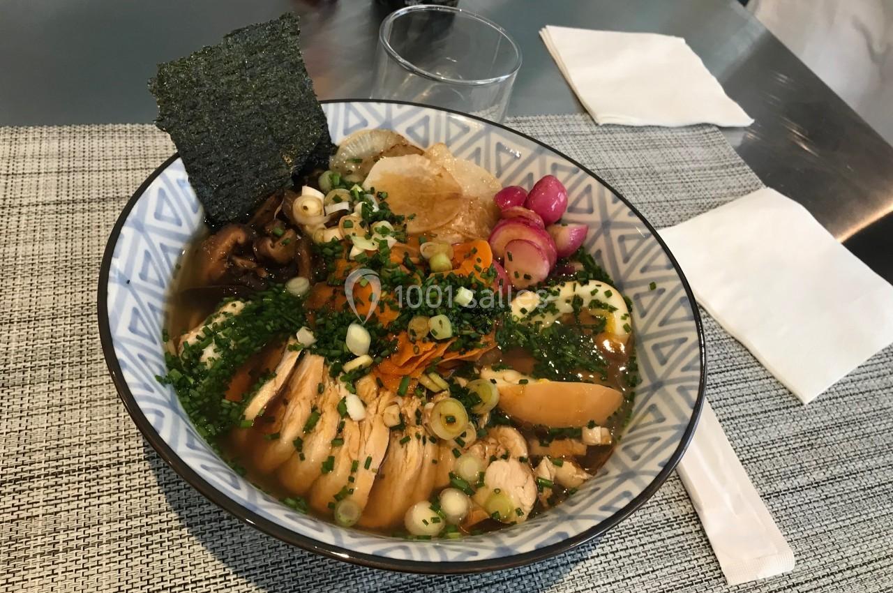 Bol de ramen garni de légumes, œuf, algue nori, ciboulette et poulet, posé sur une table avec des serviettes.