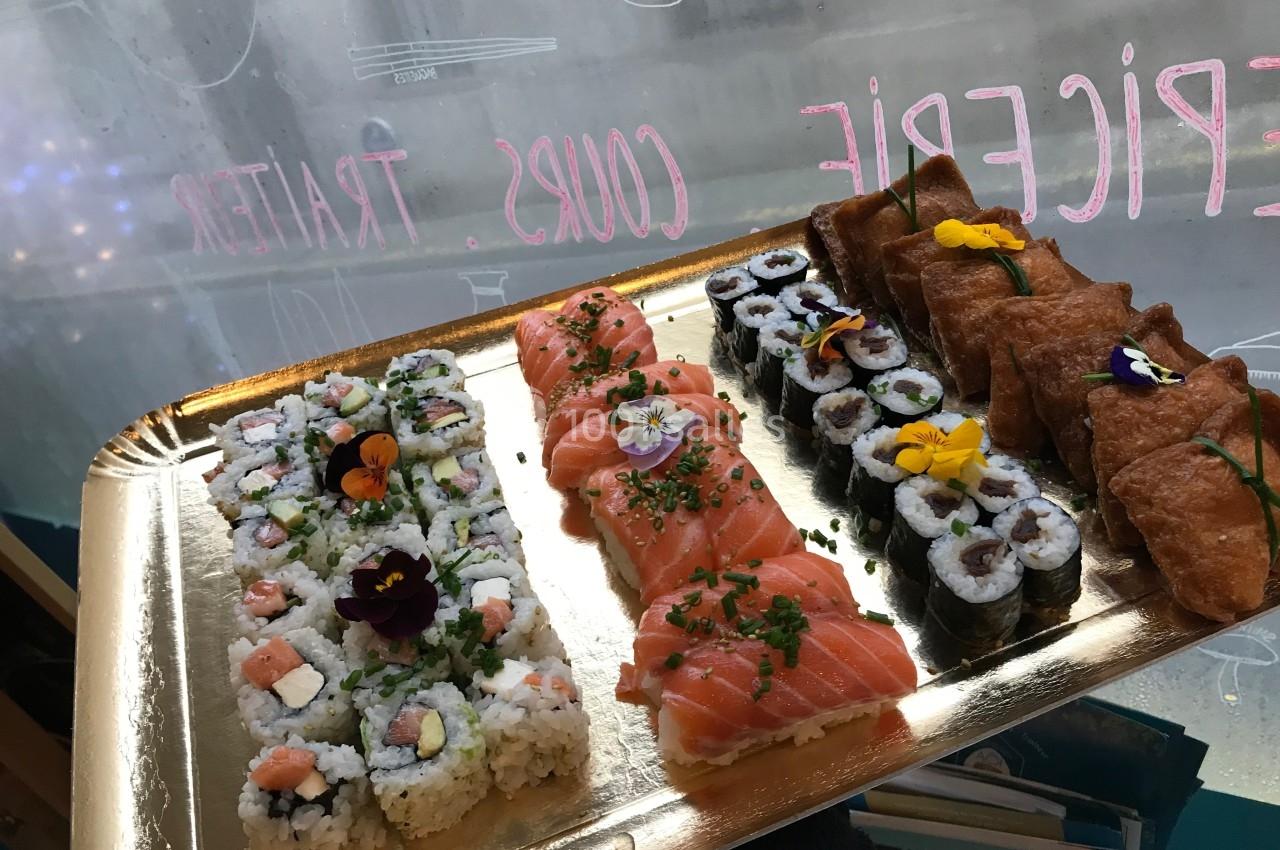 Plateau de sushis variés avec makis, nigiris et inaris décorés de fleurs comestibles, présenté sur un plateau doré.