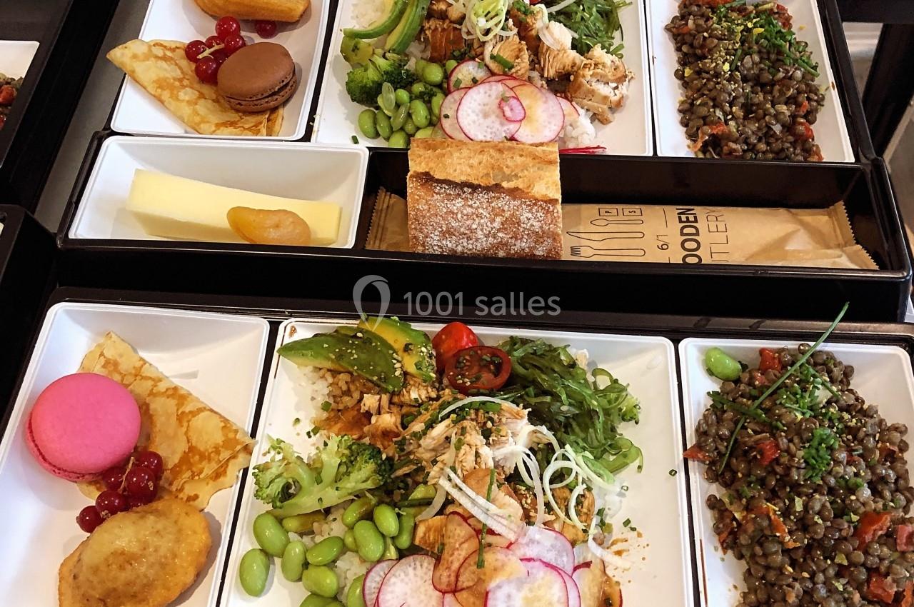 Plateaux-repas variés comprenant salade, lentilles, fromage, pain, pâtisseries et fruits, disposés sur une table.