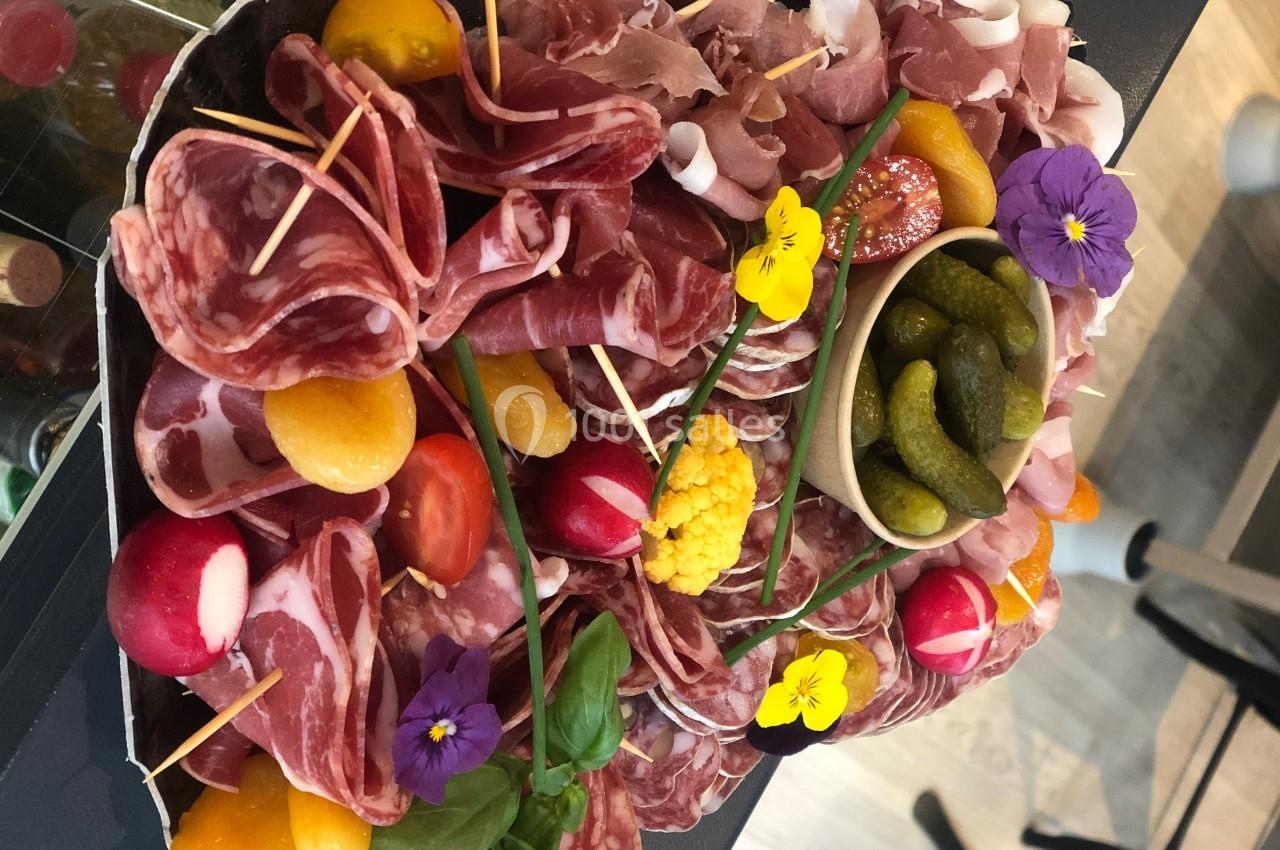Plateau de charcuterie variée avec tomates cerises, radis, cornichons, fleurs comestibles et décorations colorées.