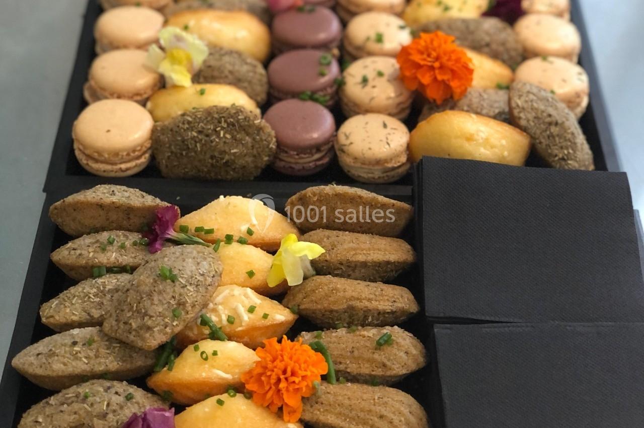 Plateau de mignardises variées comprenant macarons, madeleines et bouchées salées, décoré de fleurs comestibles.