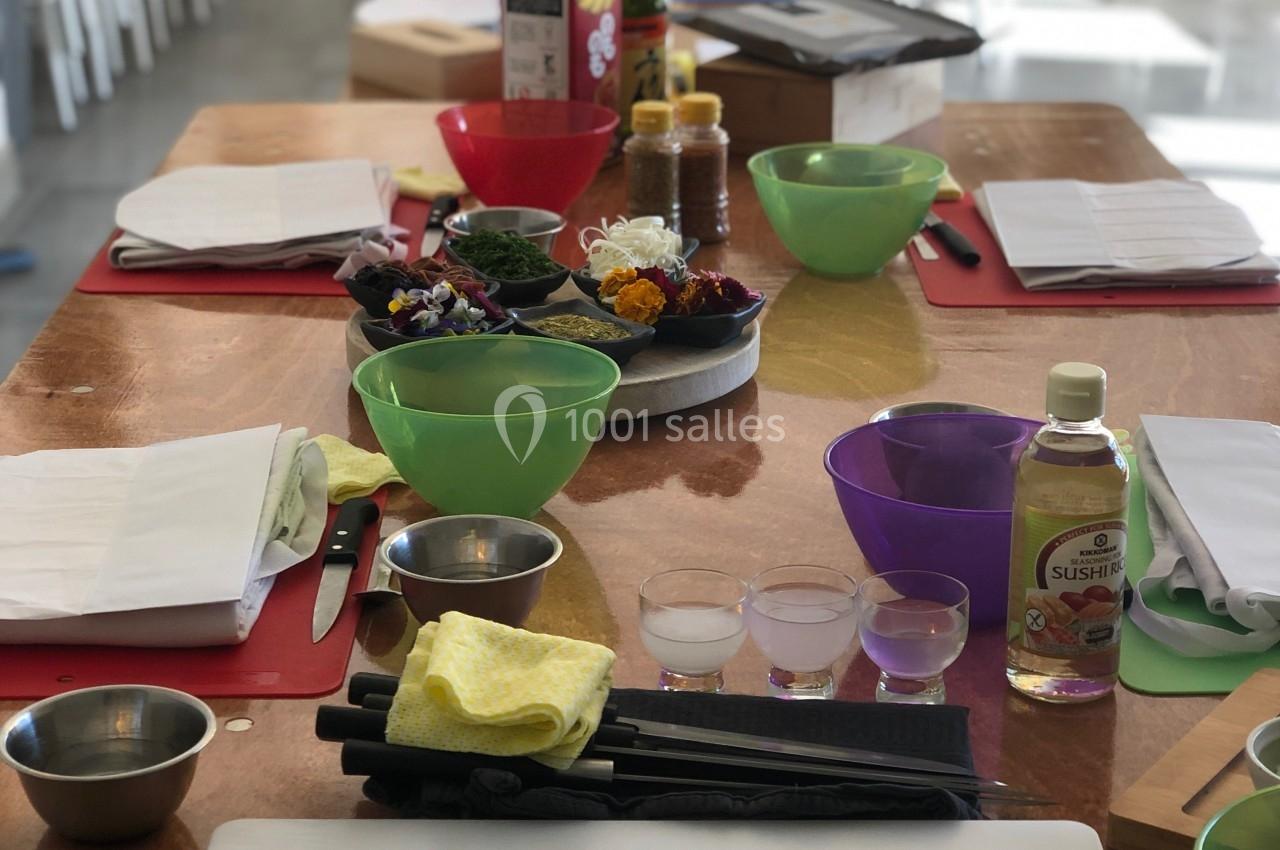 Plan de travail avec ustensiles de cuisine, planches à découper, bols et ingrédients, dans une salle lumineuse.
