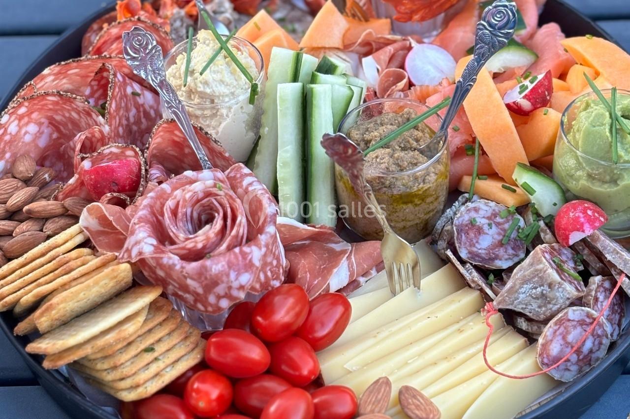 Plateau garni de charcuterie, fromages, légumes frais, fruits secs, tomates cerises et crackers sur une table en extérieur.