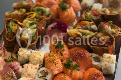 Personnes préparant des sushis autour d'une table avec des bols, ingrédients et ustensiles de cuisine.