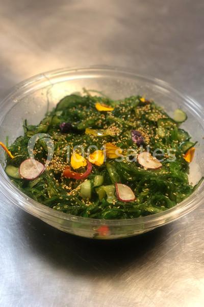 Salade de wakamé avec radis, concombre, graines de sésame et fleurs comestibles dans un bol transparent.
