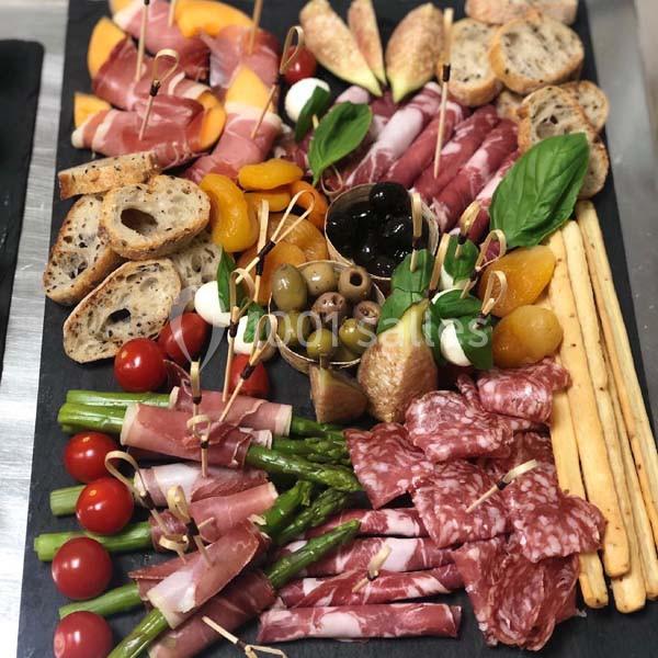 Plateau de charcuterie et fromages avec fruits, légumes, olives, pain et gressins, présenté sur une ardoise.