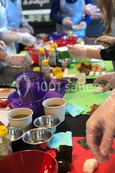 Personnes préparant des sushis autour d'une table avec des bols, ingrédients et ustensiles de cuisine.
