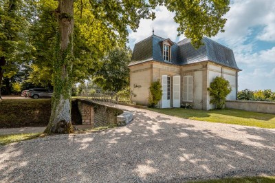 Grand bâtiment classique entouré d'une pelouse bien entretenue, avec un arbre imposant et un petit bassin au premier plan.