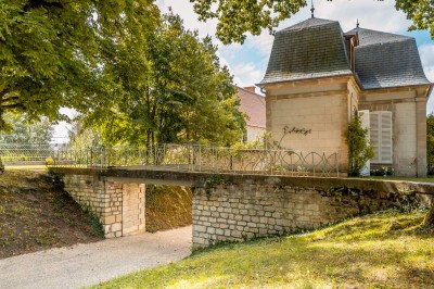 Grand bâtiment classique entouré d'une pelouse bien entretenue, avec un arbre imposant et un petit bassin au premier plan.