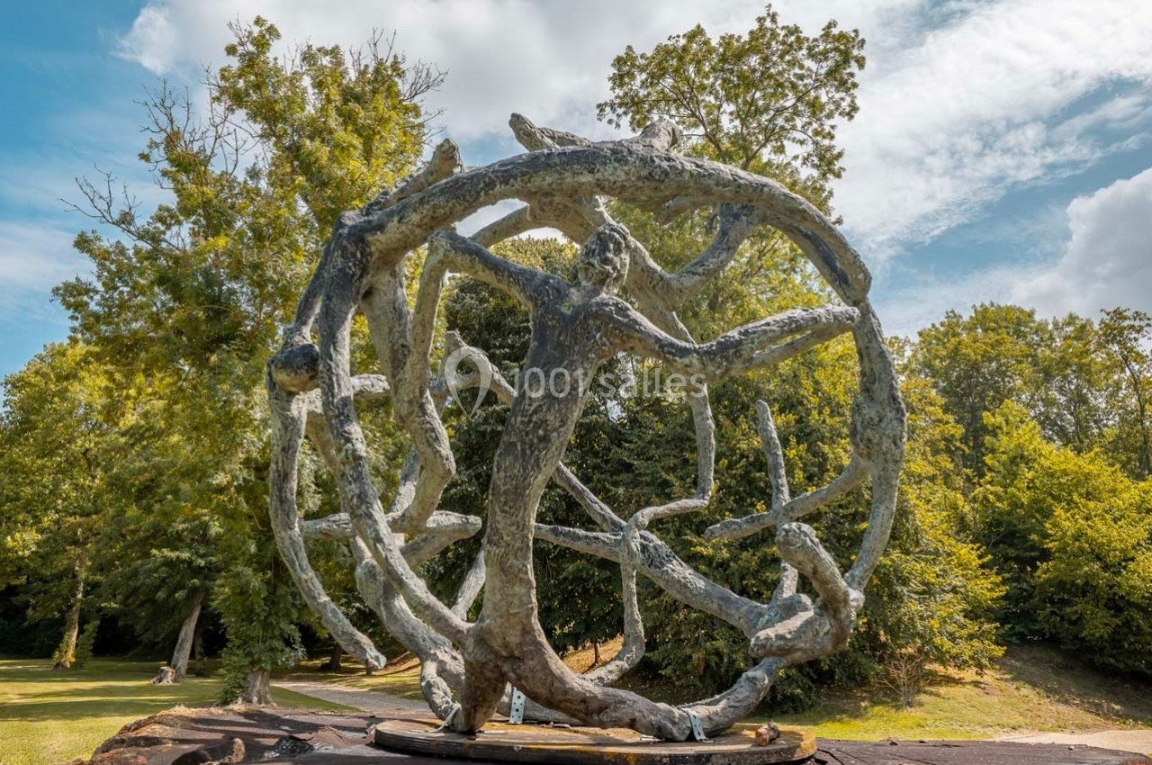 Sculpture en métal représentant des formes humaines entrelacées dans une sphère, exposée dans un parc verdoyant.
