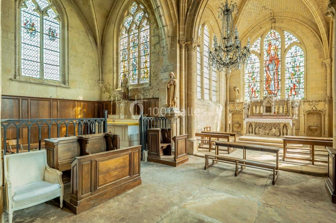 Intérieur d'une église avec autel, vitraux colorés, statues religieuses et bancs en bois sous un lustre suspendu.
