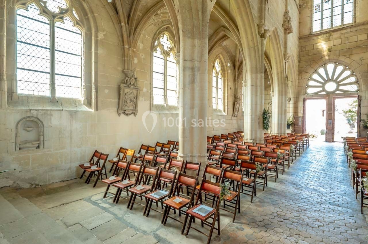 Intérieur d'une église avec des rangées de chaises en bois alignées sous des voûtes et des fenêtres gothiques.
