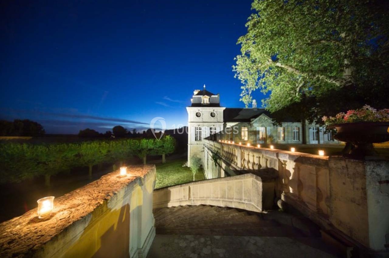 Château éclairé la nuit, entouré de vignes, avec des bougies disposées sur un muret en pierre.