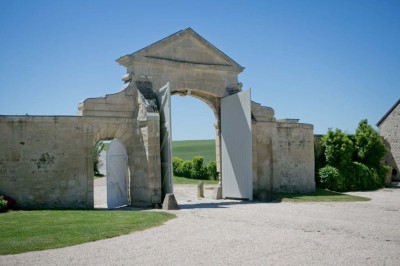 Grand bâtiment classique entouré d'une pelouse bien entretenue, avec un arbre imposant et un petit bassin au premier plan.