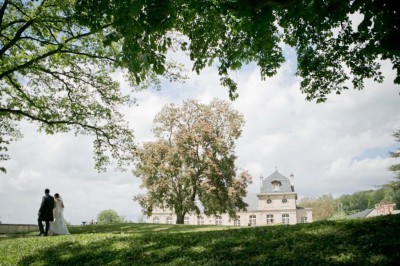 Grand bâtiment classique entouré d'une pelouse bien entretenue, avec un arbre imposant et un petit bassin au premier plan.
