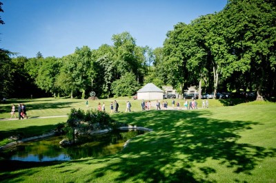 Grand bâtiment classique entouré d'une pelouse bien entretenue, avec un arbre imposant et un petit bassin au premier plan.