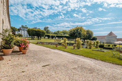 Grand bâtiment classique entouré d'une pelouse bien entretenue, avec un arbre imposant et un petit bassin au premier plan.