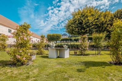 Grand bâtiment classique entouré d'une pelouse bien entretenue, avec un arbre imposant et un petit bassin au premier plan.