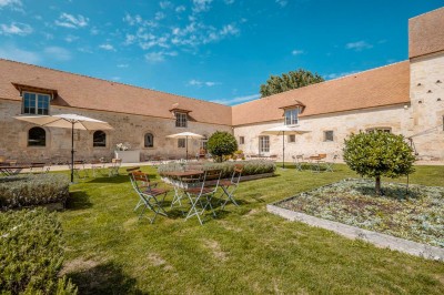 Grand bâtiment classique entouré d'une pelouse bien entretenue, avec un arbre imposant et un petit bassin au premier plan.