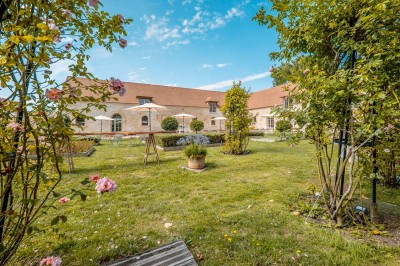 Grand bâtiment classique entouré d'une pelouse bien entretenue, avec un arbre imposant et un petit bassin au premier plan.