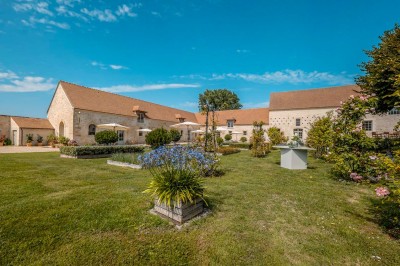 Grand bâtiment classique entouré d'une pelouse bien entretenue, avec un arbre imposant et un petit bassin au premier plan.