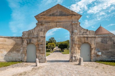 Grand bâtiment classique entouré d'une pelouse bien entretenue, avec un arbre imposant et un petit bassin au premier plan.