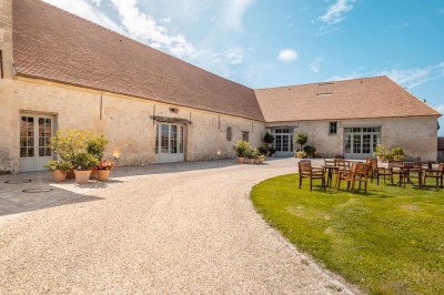 Grand bâtiment classique entouré d'une pelouse bien entretenue, avec un arbre imposant et un petit bassin au premier plan.