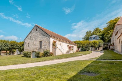 Grand bâtiment classique entouré d'une pelouse bien entretenue, avec un arbre imposant et un petit bassin au premier plan.