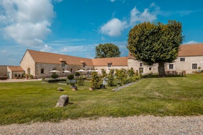 Grand bâtiment classique entouré d'une pelouse bien entretenue, avec un arbre imposant et un petit bassin au premier plan.