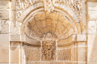 Grand bâtiment classique entouré d'une pelouse bien entretenue, avec un arbre imposant et un petit bassin au premier plan.